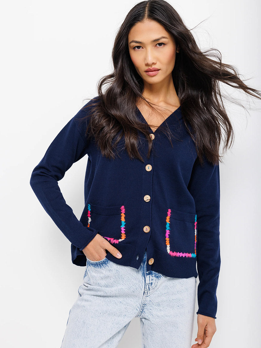 Woman posing in a Lisa Todd Rockin' Pocket Cardigan in Navy with colorful embellishments and light wash jeans.