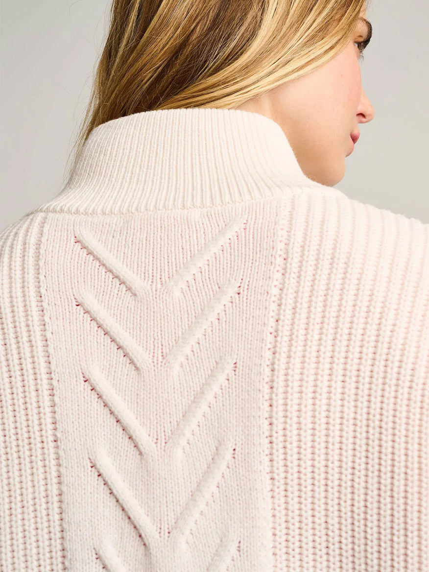A woman with blonde hair wears the Lisa Todd Rule Bender Sweater in Snow, a cream zip-up with a chevron knit back, thick folded collar, and vegan leather zipper pull.