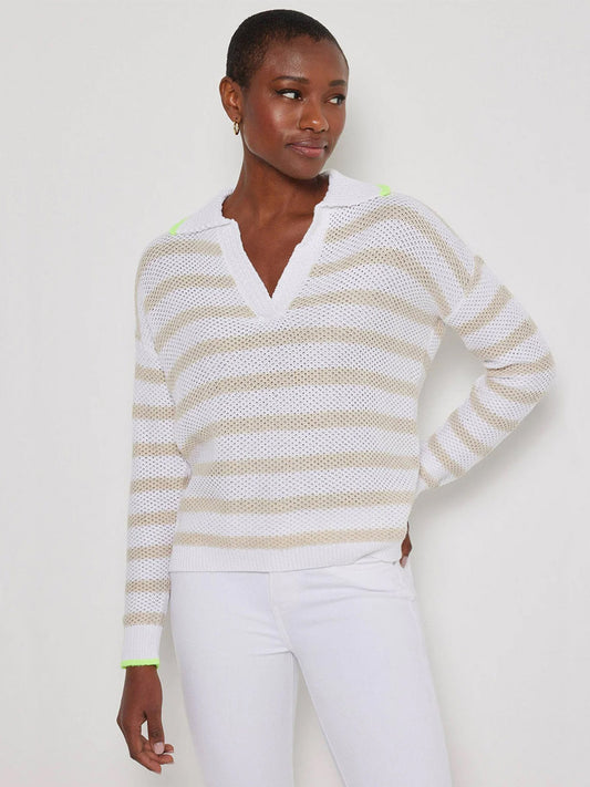 A woman wears the Lisa Todd Stripescape Collared V-Neck Sweater in White/Almond with white pants, standing against a plain light background.