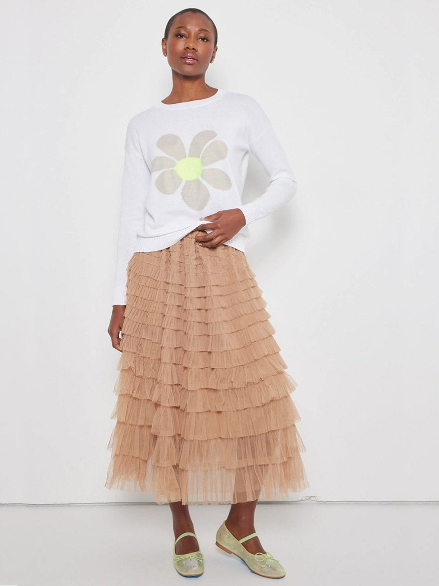 A person wearing the Lisa Todd Sweet Talk Sweater in White with an intarsia flower design and a layered beige tulle skirt stands against a plain white background.