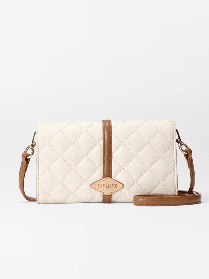 The MZ Wallace Astor Convertible Crossbody in Sandshell Oxford With Brown is a small quilted cream bag with a brown strap and trim, featuring a diamond-shaped logo patch on the front.