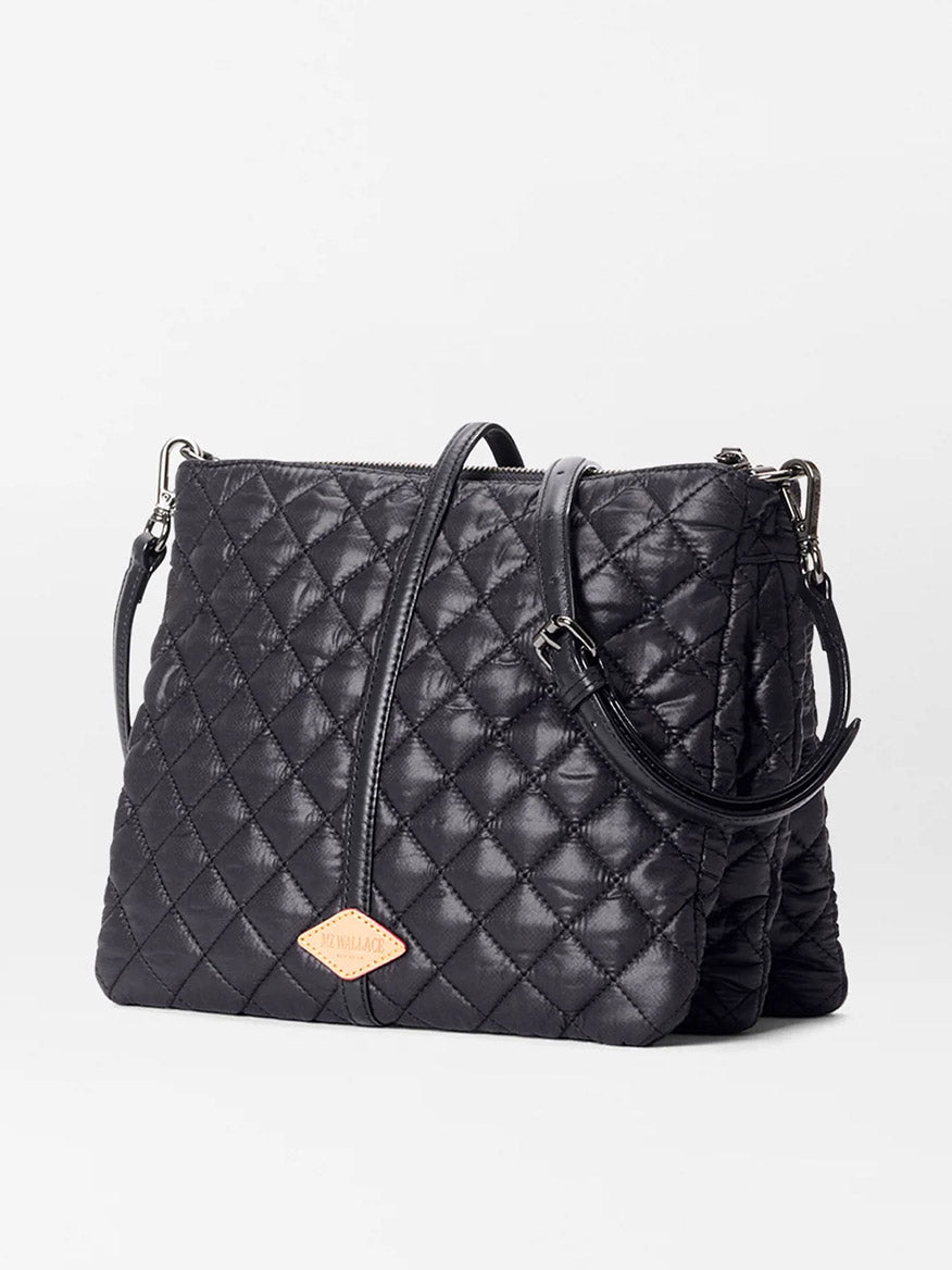 The MZ Wallace Astor Crossbody in Black Oxford features a black quilted diamond pattern, double handles, and a crossbody strap, shown against a plain light background.