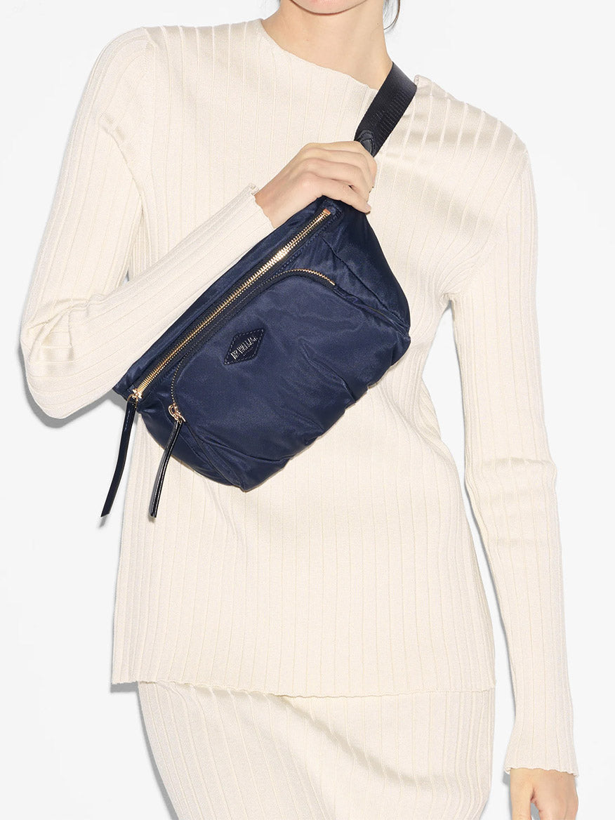 A person in a white ribbed sweater wearing a navy blue MZ Wallace Chelsea Sling Bag in Dawn Bedford made of water-repellent dawn fabric.
