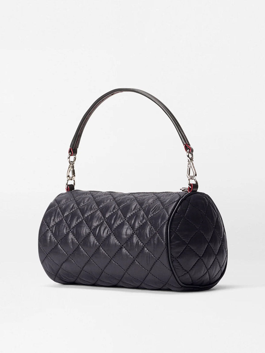 The MZ Wallace Crosby Barrel Crossbody in Black Oxford is a black, quilted cylindrical handbag with Italian leather trim, a short top handle, silver hardware, and detachable straps, shown against a plain white background.