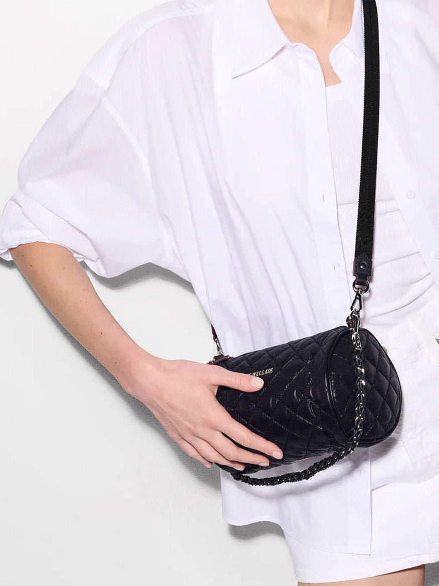 Person wearing a white shirt and holding the MZ Wallace Crosby Barrel Crossbody in Black Oxford, featuring signature hardware and a chain strap.