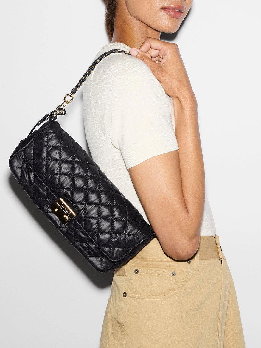 A person wearing a black MZ Wallace Crosby Lock Baguette in Black Oxford with a gold clasp and a braided chain strap.