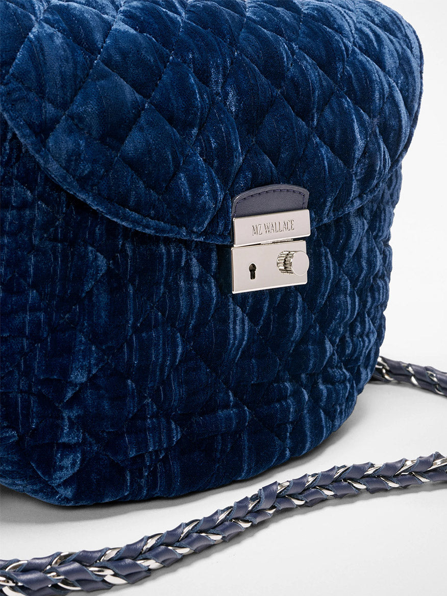 Close-up of the MZ Wallace Crosby Lock Saddle in Midnight Velvet, a quilted dark blue velvet crossbody with silver clasp and braided strap. Features detachable strap for versatile wear and "MZ Wallace" engraved on the clasp.