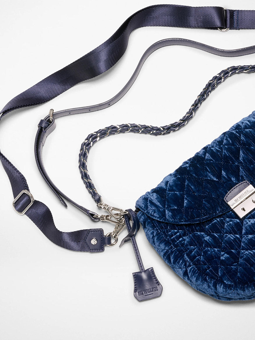 The MZ Wallace Crosby Lock Saddle in Midnight Velvet is a blue quilted velvet crossbody bag with a silver clasp, chain detailing, and an adjustable shoulder strap, displayed on a white surface.