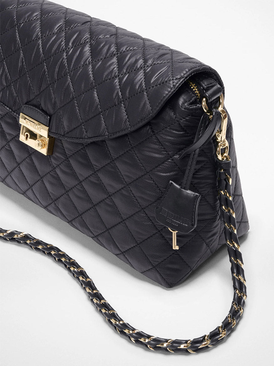 The MZ Wallace Crosby Lock Shoulder in Black Oxford is a black quilted crossbody bag with a gold clasp, a chain strap woven with Italian leather, and a small leather key holder by the zipper.