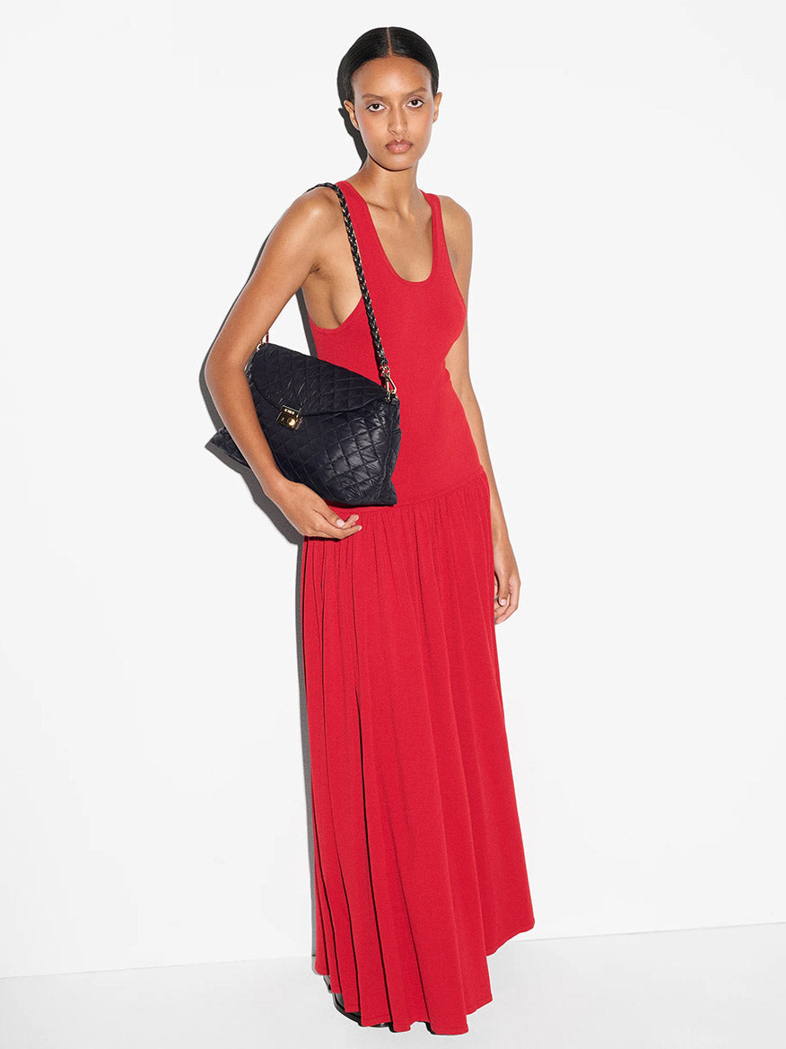 A person in a sleeveless red dress stands against a white background, holding the MZ Wallace Crosby Lock Shoulder in Black Oxford, featuring an Italian leather strap.