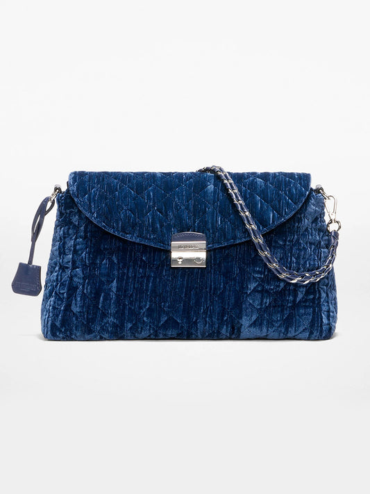 The MZ Wallace Crosby Lock Shoulder in Midnight Velvet is a blue quilted velvet handbag with a silver flap closure and detachable chain strap, shown against a plain white background.