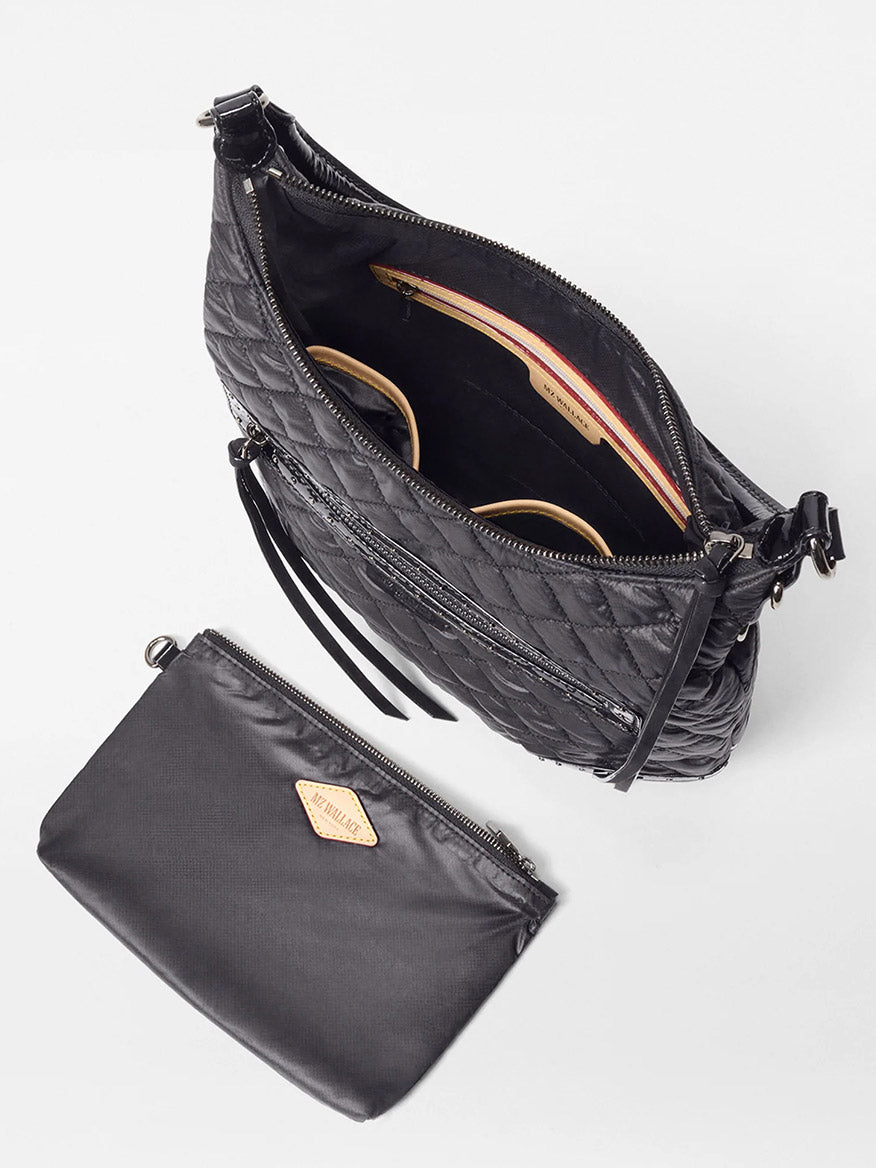 The MZ Wallace Multi Stud Crosby Sienna in Black Stud & Suede is shown unzipped to reveal sunglasses and another item inside, next to its matching zippered pouch with Italian leather trim, all displayed on a white background.