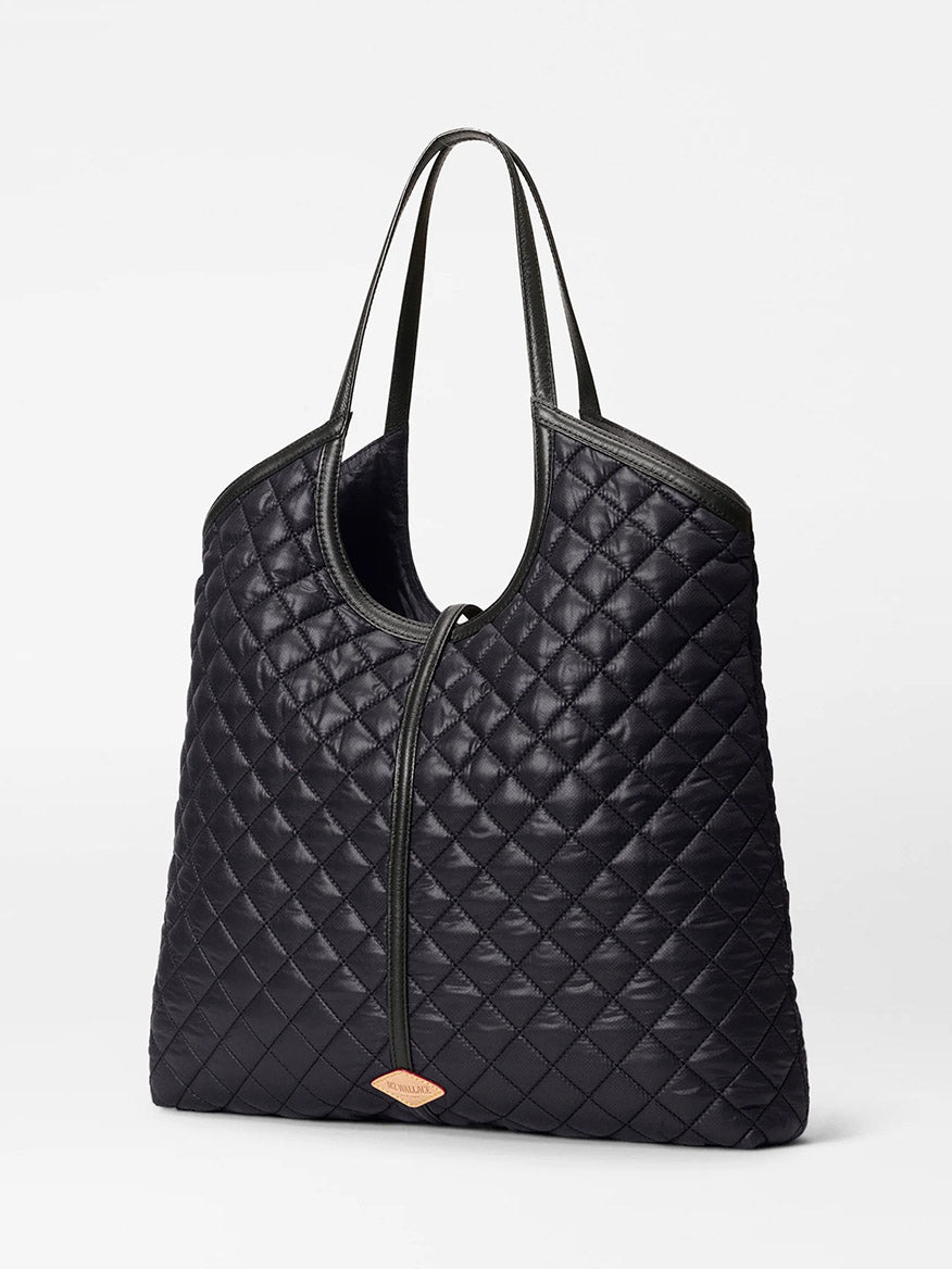 The MZ Wallace Large Astor Tote in Black Oxford features quilted fabric, Italian leather handles, and a small tan label on the lower front, shown against a plain white background.