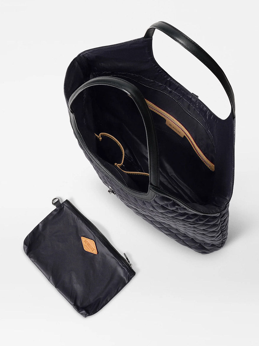 The MZ Wallace Large Astor Tote in Black Oxford is shown from above, featuring quilted fabric, Italian leather handles, an open interior, and a detachable zippered pouch placed beside it.