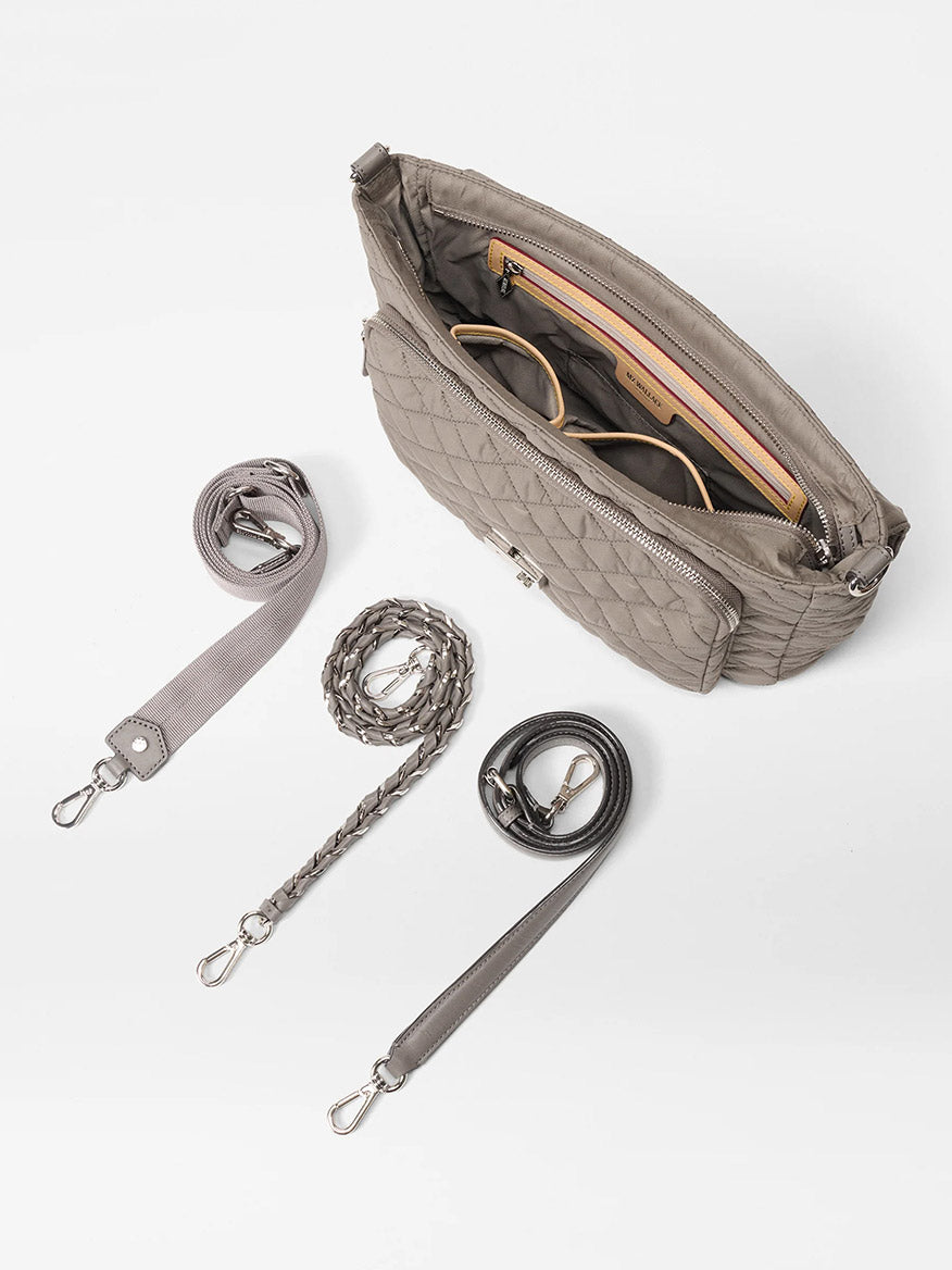 The MZ Wallace Crosby Lock Large Crossbody in Morning Dove Oxford is shown on a white background, featuring nylon quilting, three detachable straps, and includes a pair of sunglasses inside.