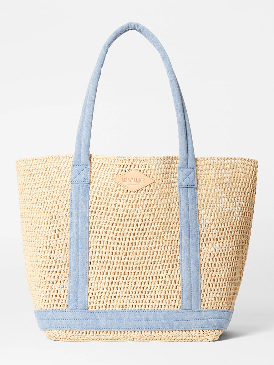 The MZ Wallace Medium Crochet Tote in Crochet/True Light Denim is a beige woven tote with padded nylon handles, blue trims, and a front natural Italian leather patch.