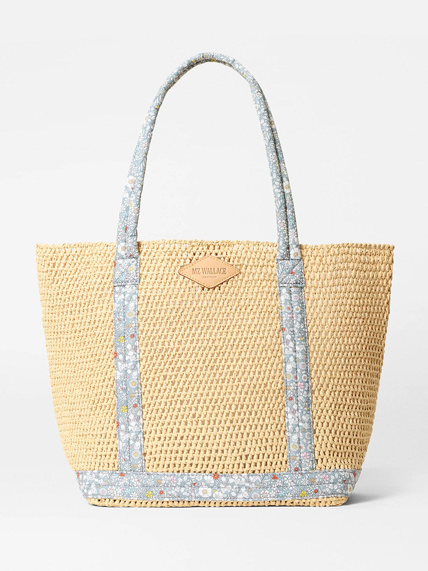 The MZ Wallace Medium Crochet Tote features a woven straw design with two blue June's Meadow Liberty Fabric floral handles, matching trim, and a small Italian leather logo patch on the front.