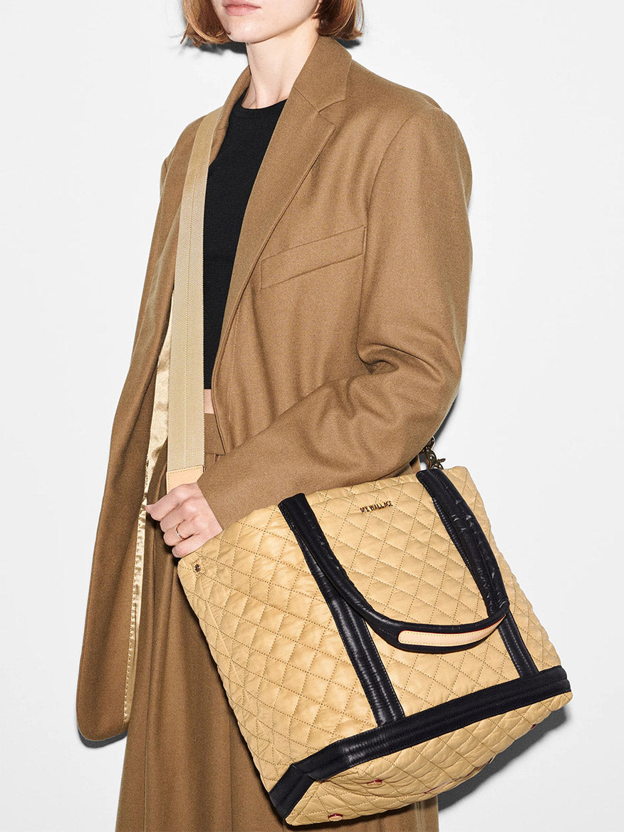 A woman in a MZ Wallace Medium Empire Tote in Camel & Black holding a large quilted spacious tote with black trim.