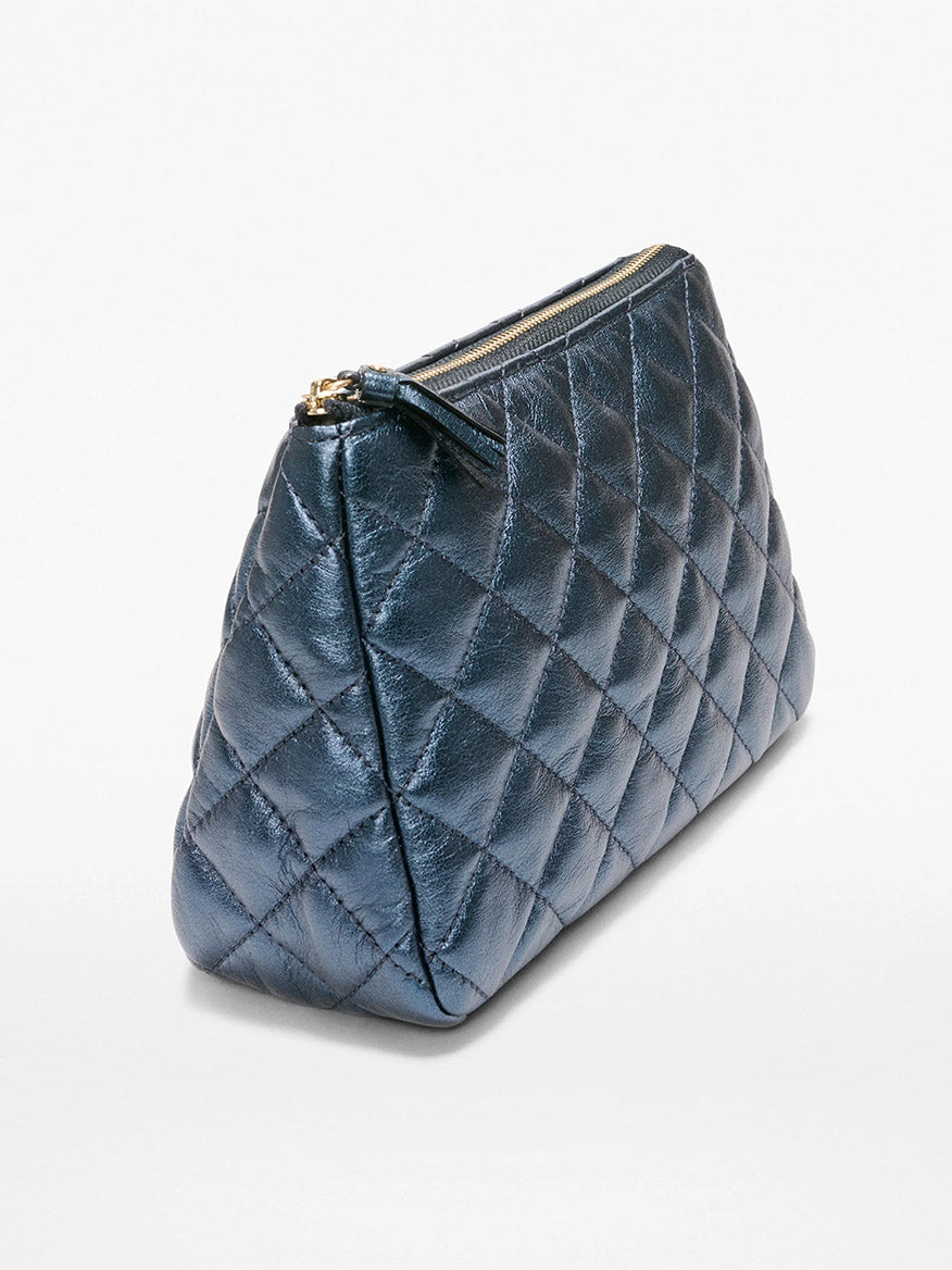 The MZ Wallace Medium Luna Cosmetic in Midnight Metallic Leather features dark blue quilted Italian leather, light gold hardware, and a zipper closure, shown at an angle on a plain white background.