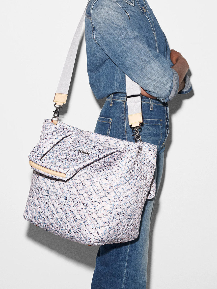 A person in denim attire carrying a MZ Wallace Medium Metro Tote Deluxe in Summer Shale Oxford with a white strap.