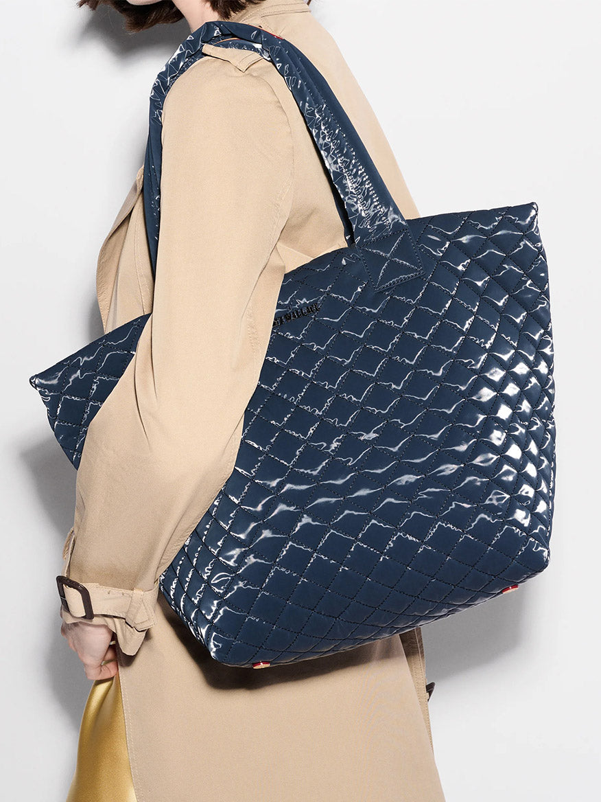 A person in a beige coat carries the MZ Wallace Medium Metro Tote Deluxe in Ink Liquid Oxford over their shoulder.
