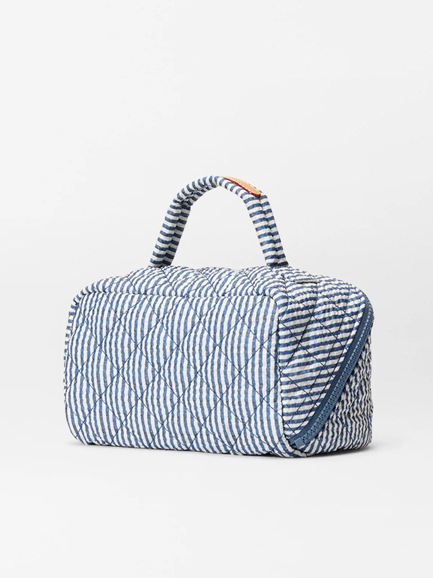 The MZ Wallace Metro Accordion Cosmetic in Seersucker Oxford is a quilted, rectangular nylon makeup bag with blue and white stripes, a top handle, and side zip closure—ideal for travel organization.