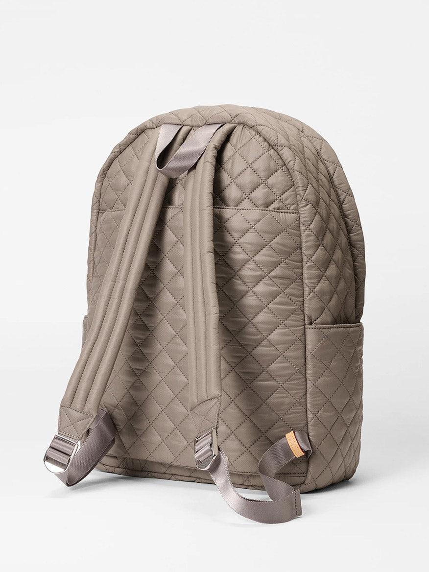 The MZ Wallace Metro Backpack II in Morning Dove Oxford, a taupe quilted laptop backpack with padded shoulder straps, side pockets, and Italian leather trim, is displayed against a plain white background.