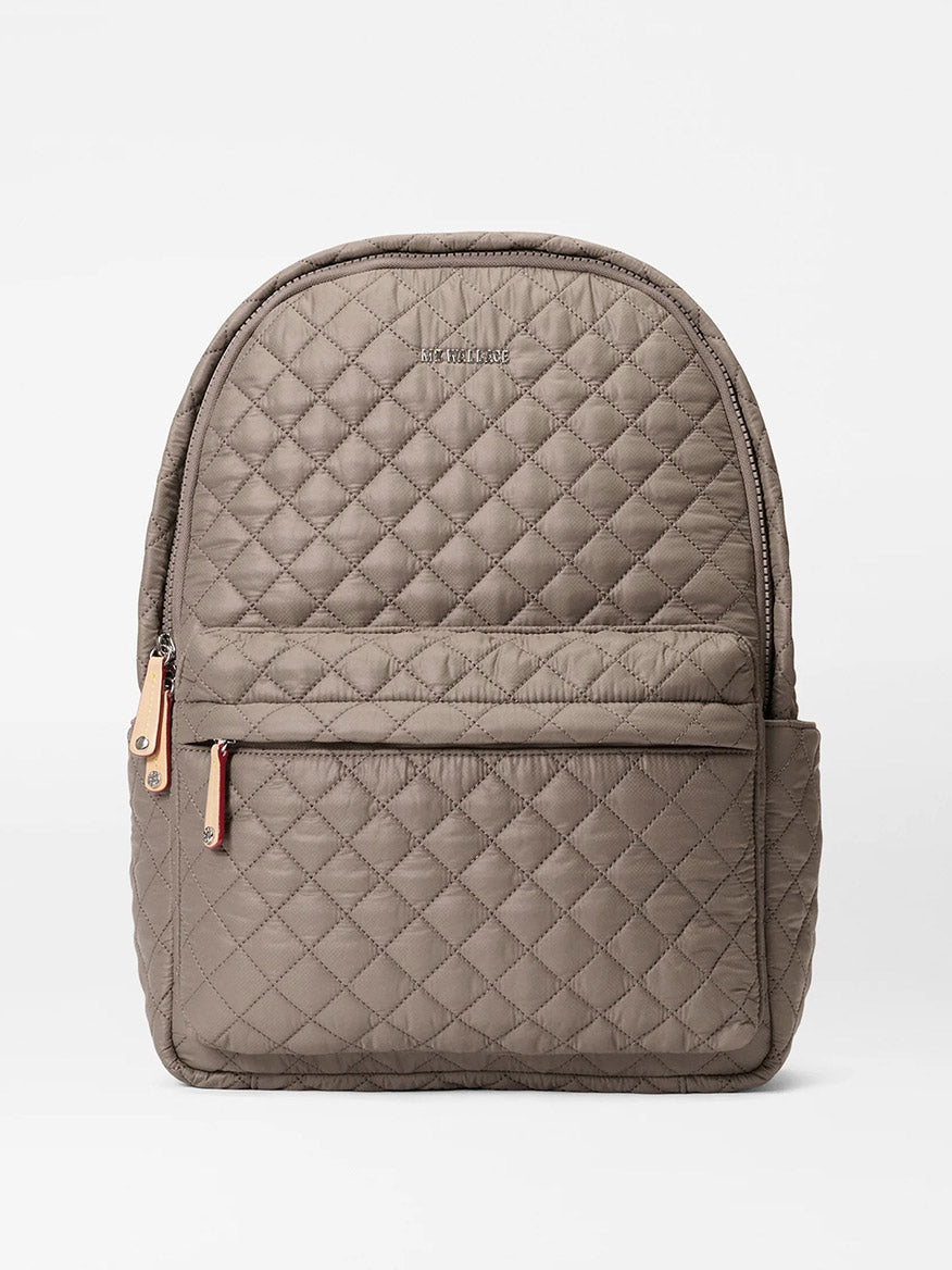 The MZ Wallace Metro Backpack II in Morning Dove Oxford, shown on a plain white background, features quilted taupe fabric, Italian leather trim, a front zip pocket, side pocket, top zipper closure, and a luggage sleeve.