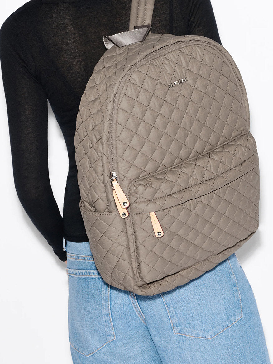 Person wearing the MZ Wallace Metro Backpack II in Morning Dove Oxford with tan zipper pulls, styled with a black top and light blue jeans, shown from the back.