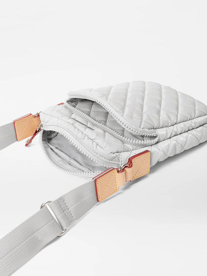A light gray quilted fabric MZ Wallace Metro Crossbody in Pebble Liquid Oxford with an adjustable crossbody strap and beige strap details on a white background.