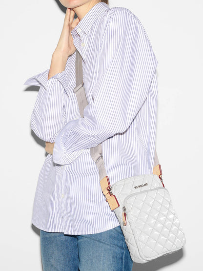 A person modeling a striped shirt with a white MZ Wallace Metro Crossbody in Pebble Liquid Oxford featuring an adjustable crossbody strap and blue jeans against a white background.