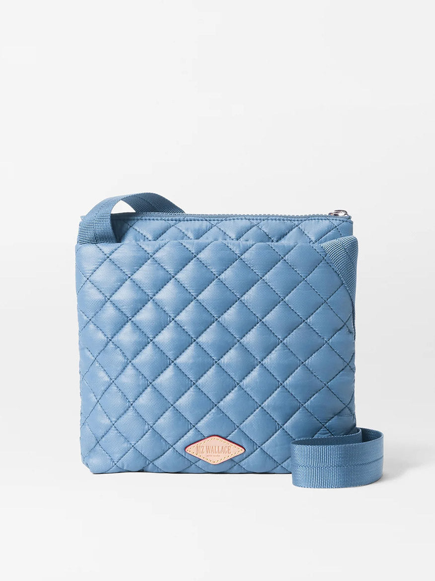Light blue quilted MZ Wallace Metro Flat Crossbody in Cornflower Blue Oxford with a zipper closure, an adjustable strap, and a branded label.