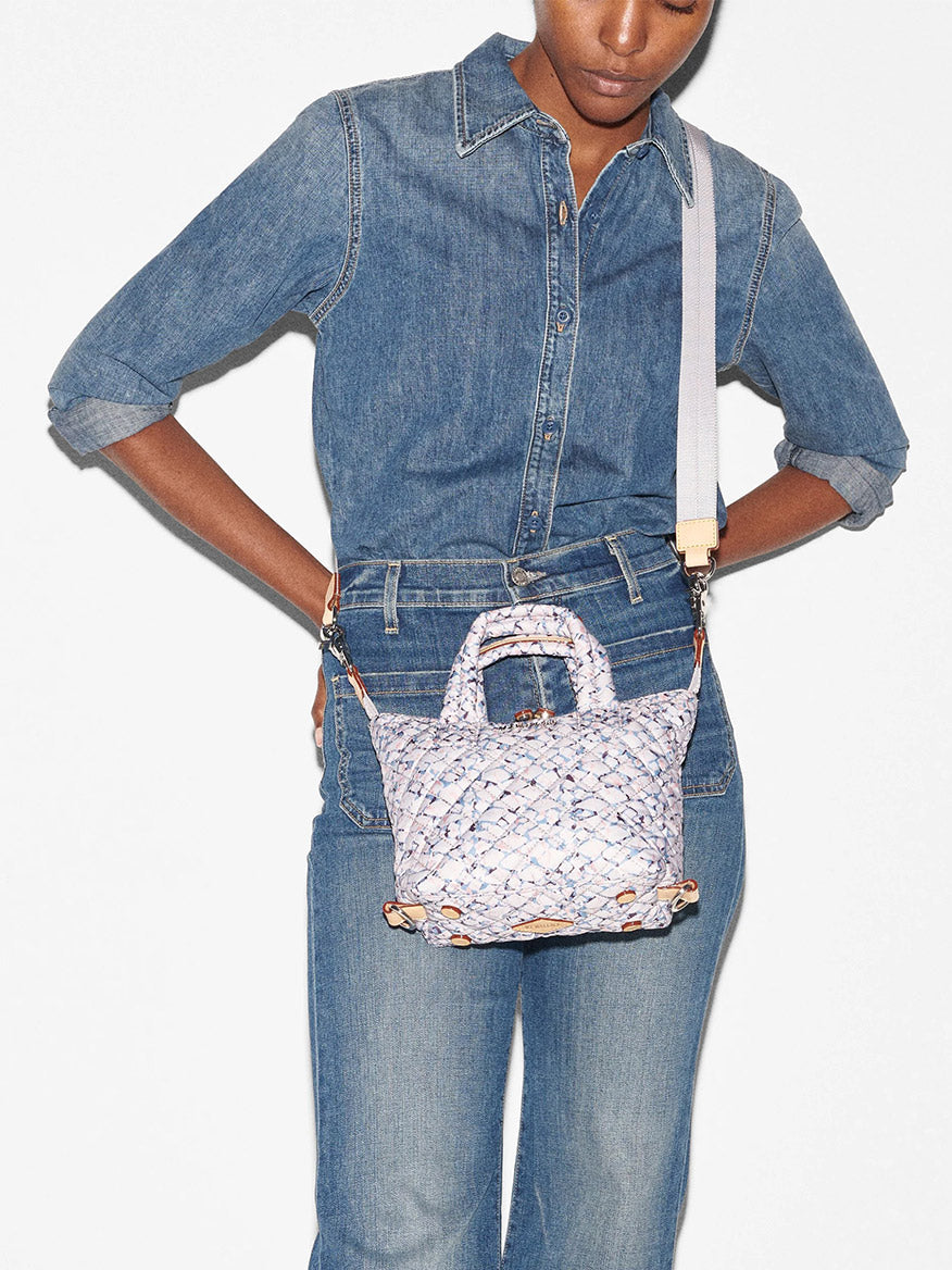 A person in a denim outfit holding a MZ Wallace Micro Sutton in Summer Shale Oxford with a crossbody strap.