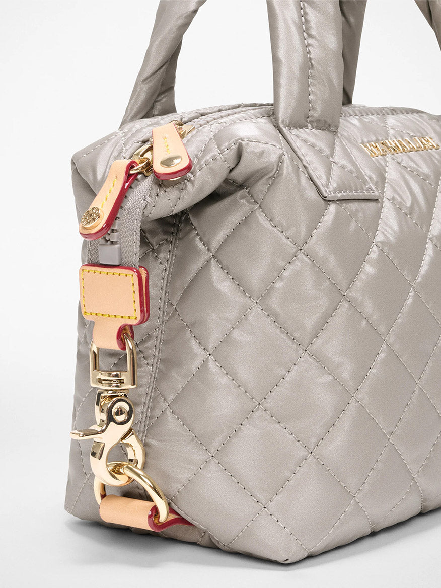 Close-up of the MZ Wallace Micro Sutton in Sable Pearl Metallic Oxford, a quilted gray handbag with gold hardware, zipper closure, metal clasp on the side, and a sleek crossbody strap for versatile carrying.