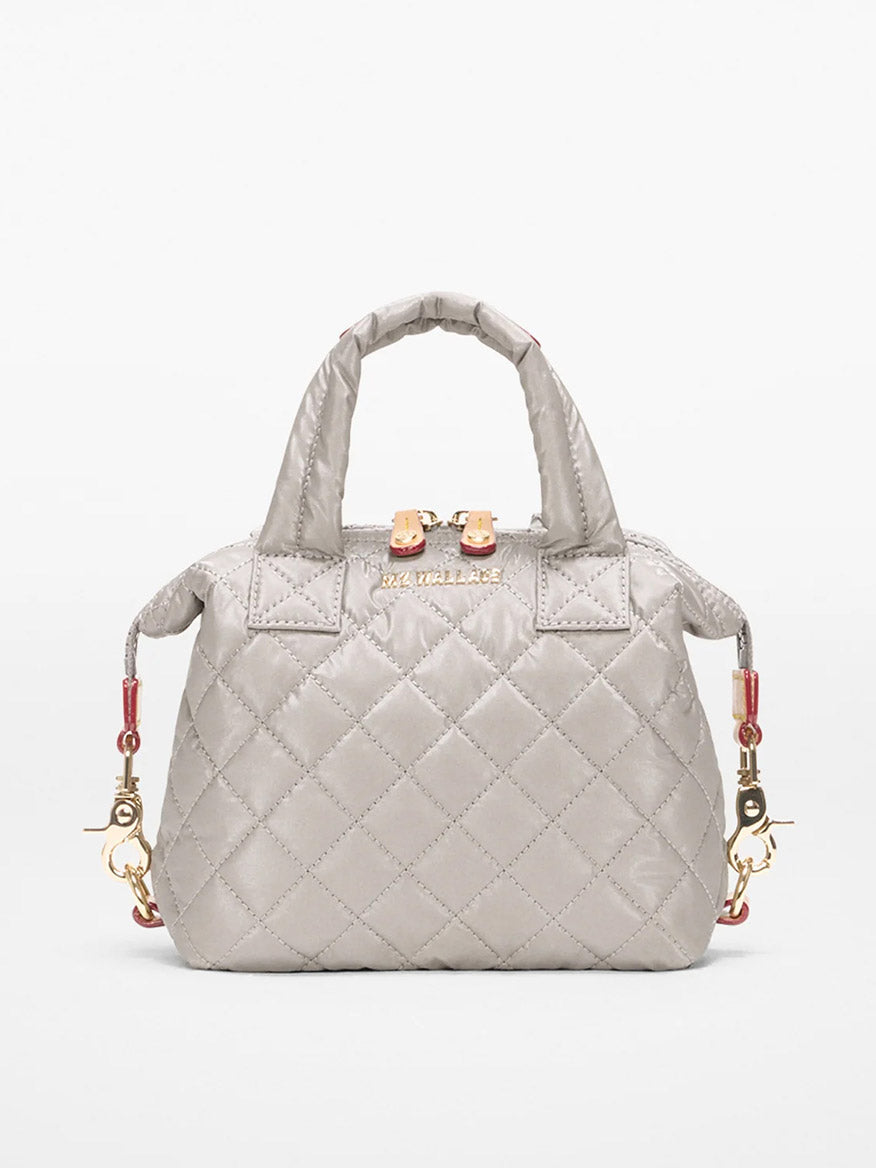 The MZ Wallace Micro Sutton in Sable Pearl Metallic Oxford is a small quilted gray handbag with gold hardware, short handles, and decorative side clasps, shown against a plain light background.