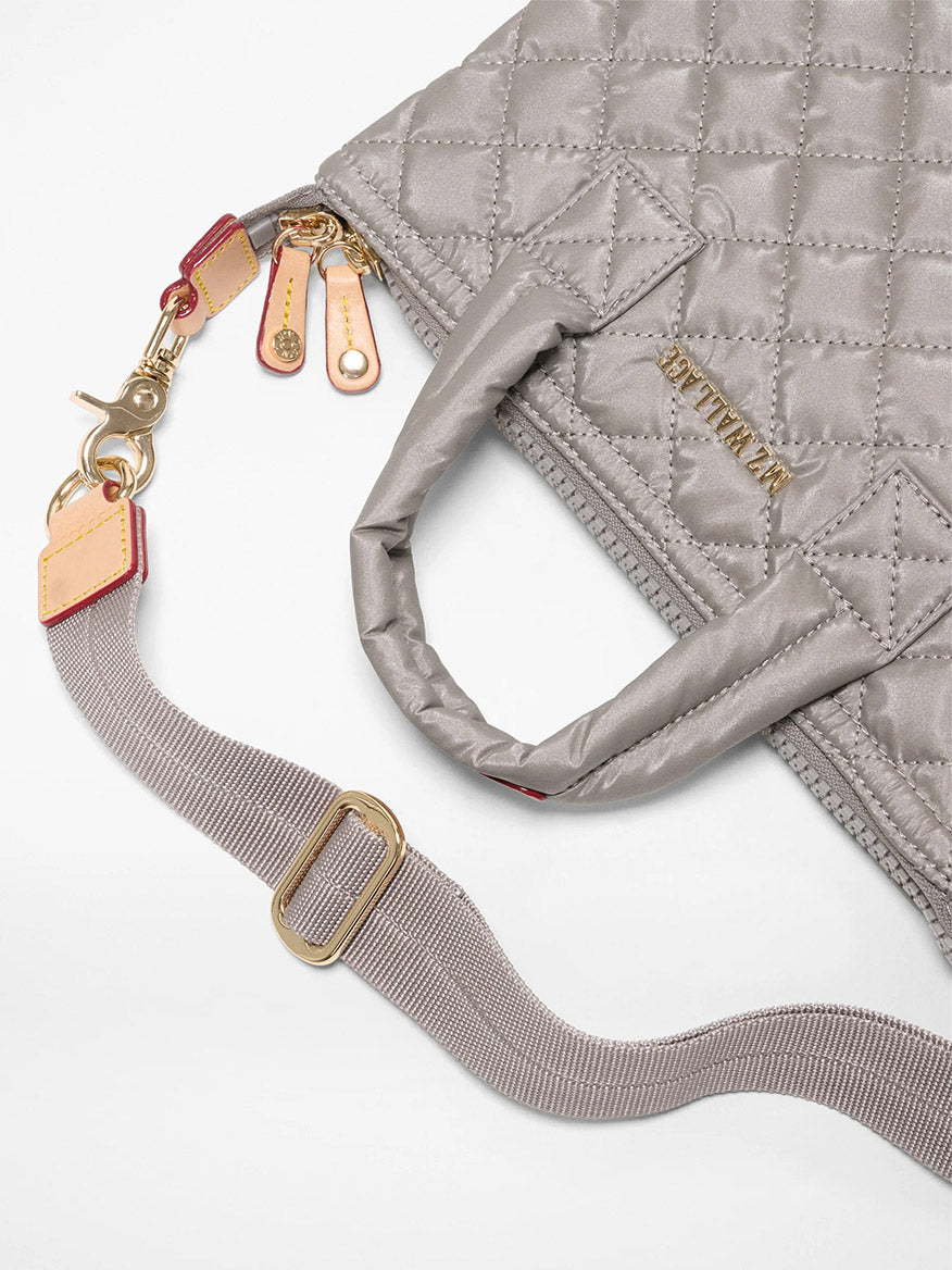A close-up of the MZ Wallace Micro Sutton in Sable Pearl Metallic Oxford, featuring gray quilting, gold zipper pulls, light brown Italian leather accents, and an adjustable gray fabric crossbody strap.