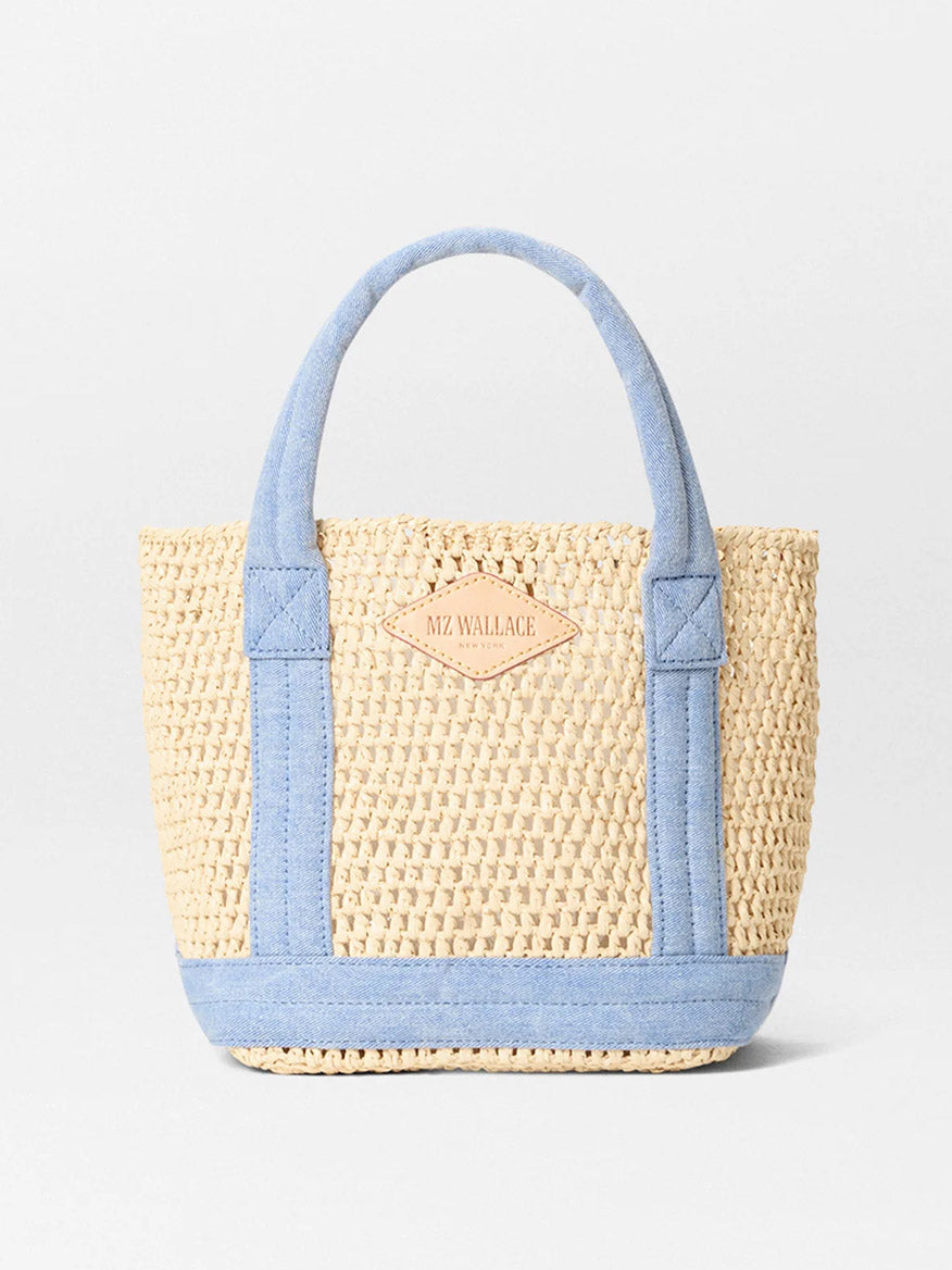 The MZ Wallace Mini Crochet Tote in Crochet/True Light Denim features woven straw with light blue fabric handles and trim, plus a small leather patch for branding. Its sophisticated Italian leather accents blend rustic charm with modern elegance.