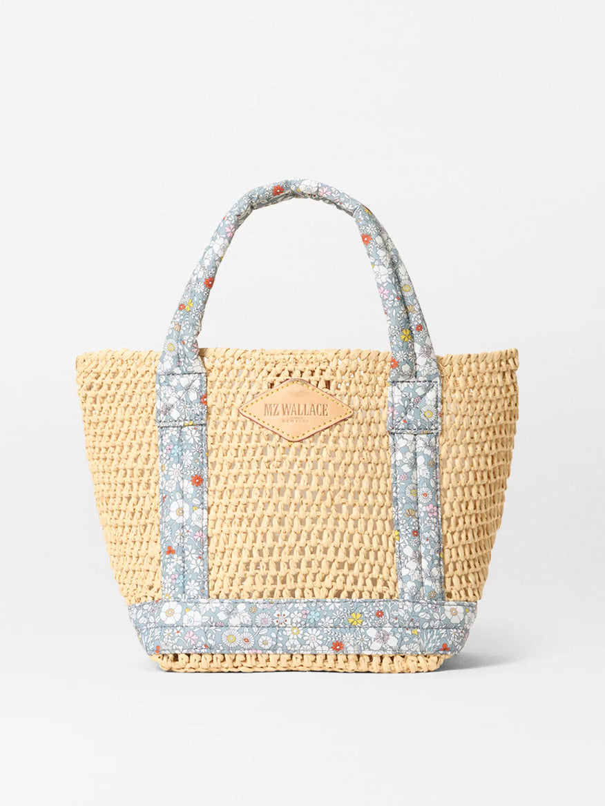 The MZ Wallace Mini Crochet Tote features a woven straw design, June's Meadow Liberty floral fabric handles, and Italian leather trim with a tan embossed leather patch on the front.