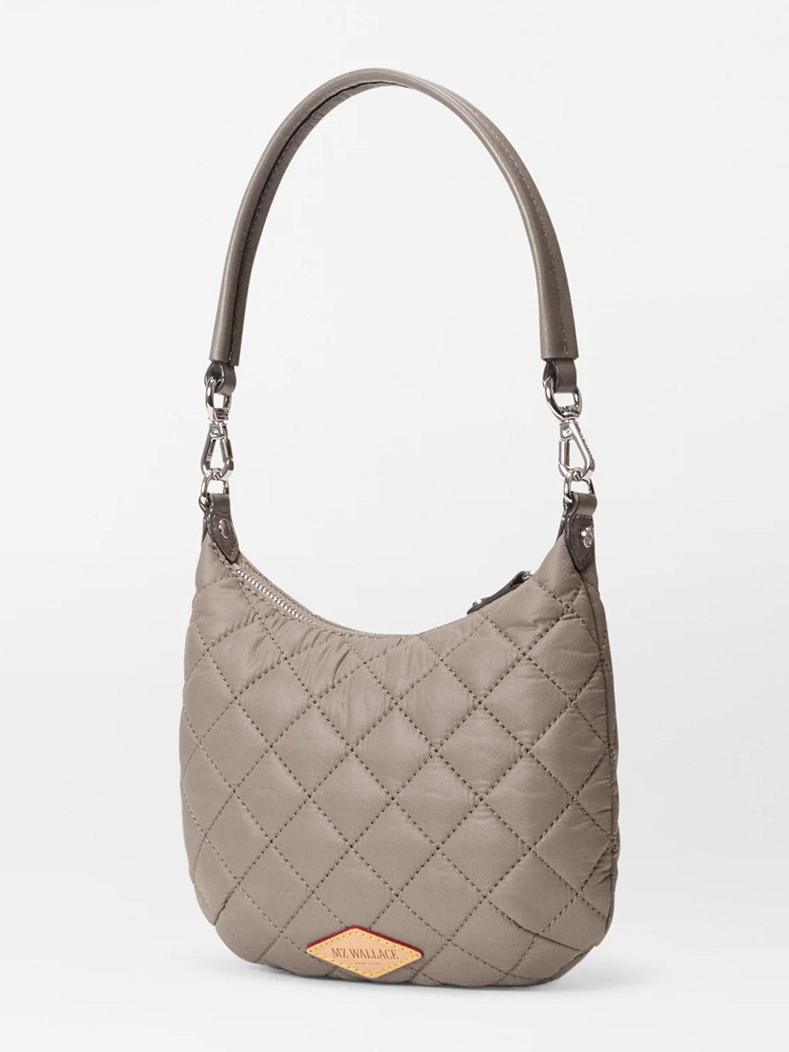 The MZ Wallace Mini Crosby Sienna in Morning Dove Oxford is a taupe quilted satchel with a short handle, silver hardware, and a tan tag featuring the brand’s logo—perfect for everyday use.