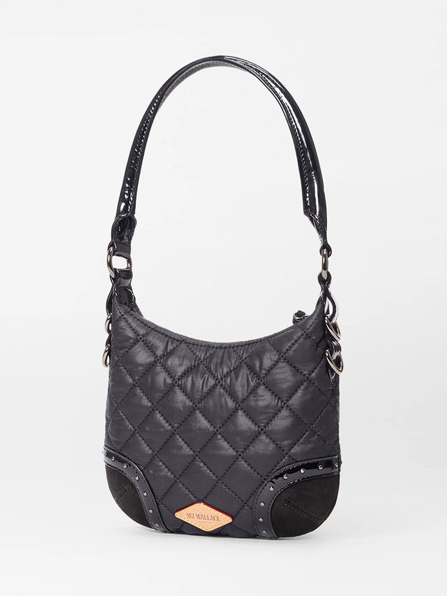 The MZ Wallace Mini Multi Stud Crosby Sienna in Black Stud & Suede is a small black quilted handbag with a curved handle, zip top closure, metallic accents, and a tan front label, shown against a plain white background.