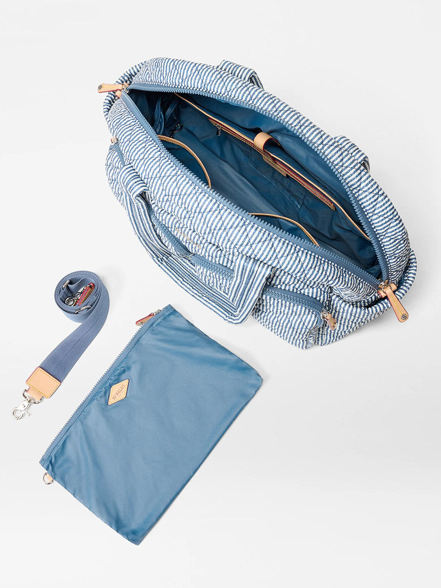 The MZ Wallace Nik Duffel in Seersucker Oxford features blue and white stripes, an open top with compartments, a detachable shoulder strap, and a matching zippered pouch—ideal for weekend getaways.