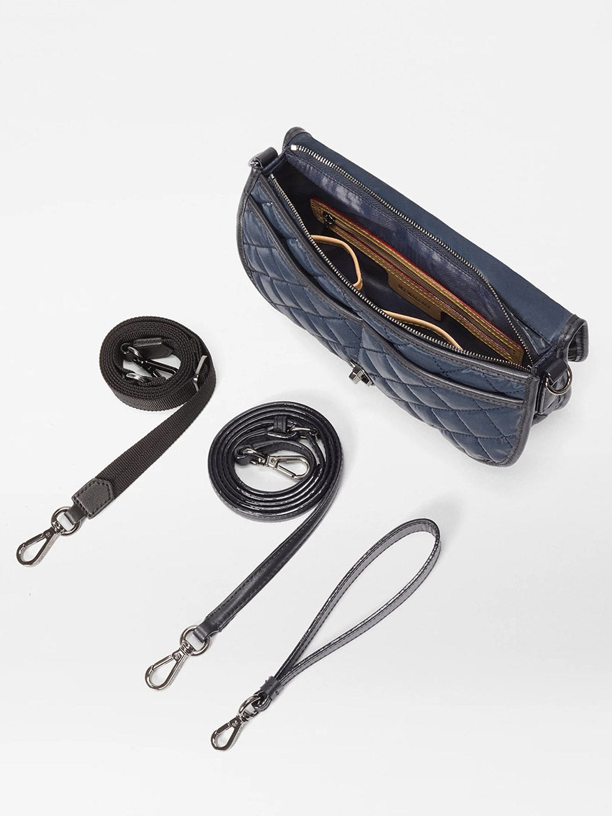 The MZ Wallace Small Astor Convertible Clutch in Ink Liquid Oxford is shown with its zipper open to reveal the interior, displayed alongside three detachable and adjustable straps of different lengths and materials on a white background.