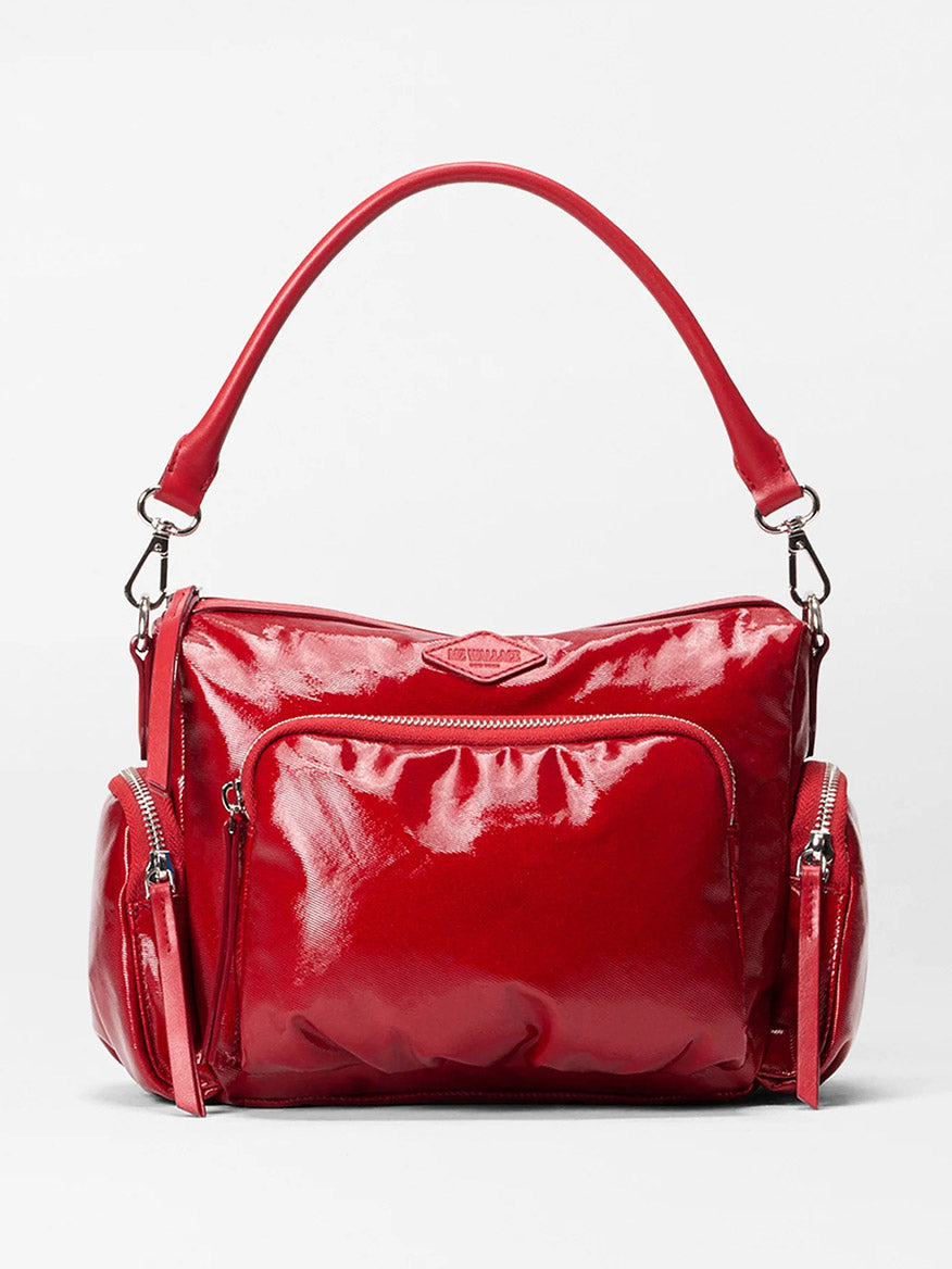 The MZ Wallace Small Chelsea Crossbody in Apple Gloss Bedford, featuring a shiny red finish, top handle, adjustable strap, front zip pocket, and two side zip pockets, is displayed against a plain light background.