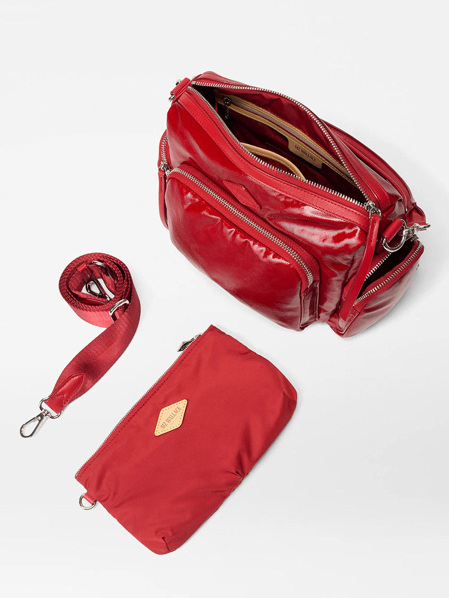 The MZ Wallace Small Chelsea Crossbody in Apple Gloss Bedford is shown with its compartments open, featuring an adjustable strap and a matching red zippered pouch, all displayed on a white background.