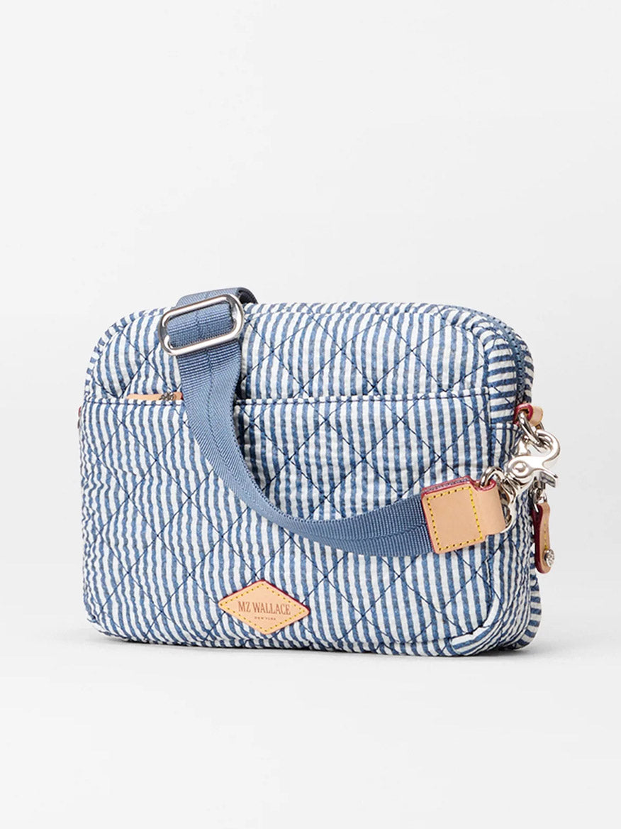 The MZ Wallace Small Metro Camera Bag in Seersucker Oxford features quilted blue-and-white striped nylon, a blue adjustable strap, leather accents, and a front "MZ Wallace" logo patch—perfect as a stylish everyday crossbody.