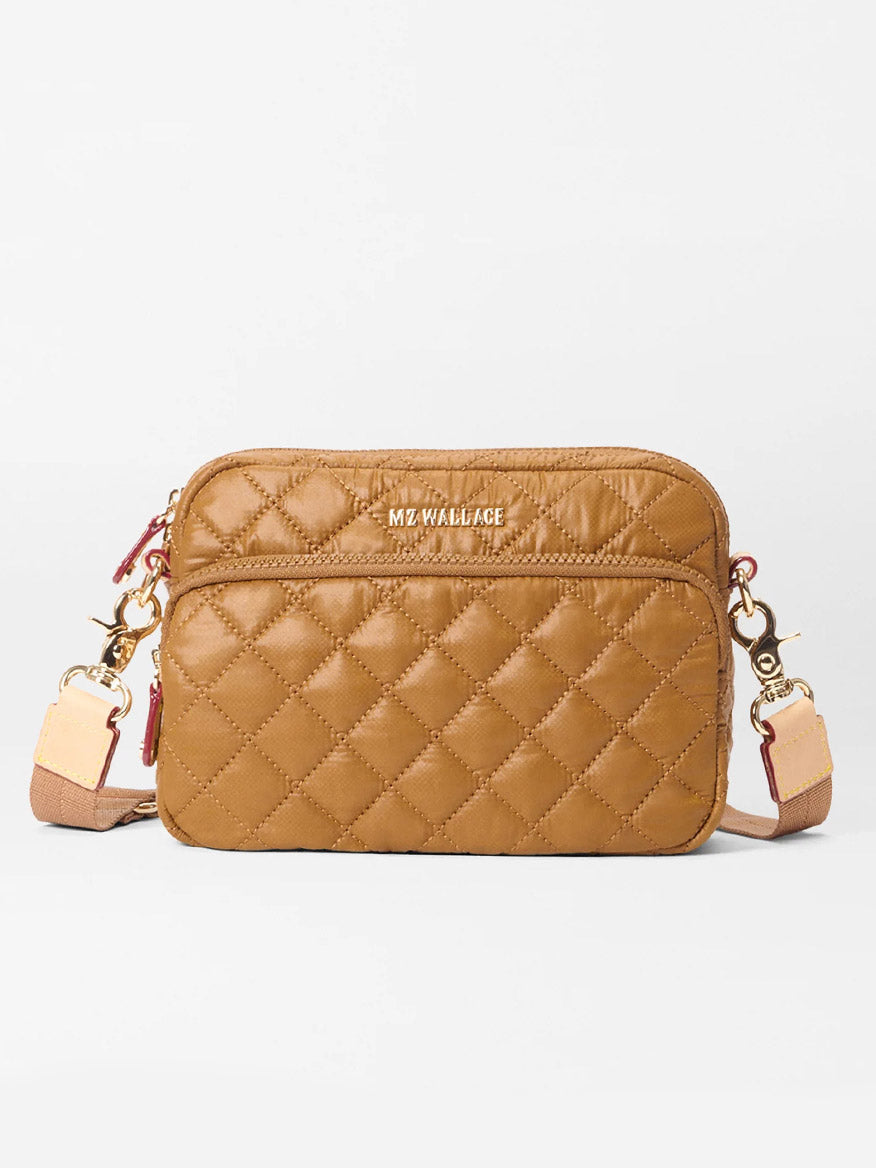 The MZ Wallace Small Metro Camera Bag in Amber Oxford features a tan quilted lightweight nylon design, gold-tone hardware, front zip pocket, adjustable strap, and "MZ WALLACE" in gold lettering on the front.