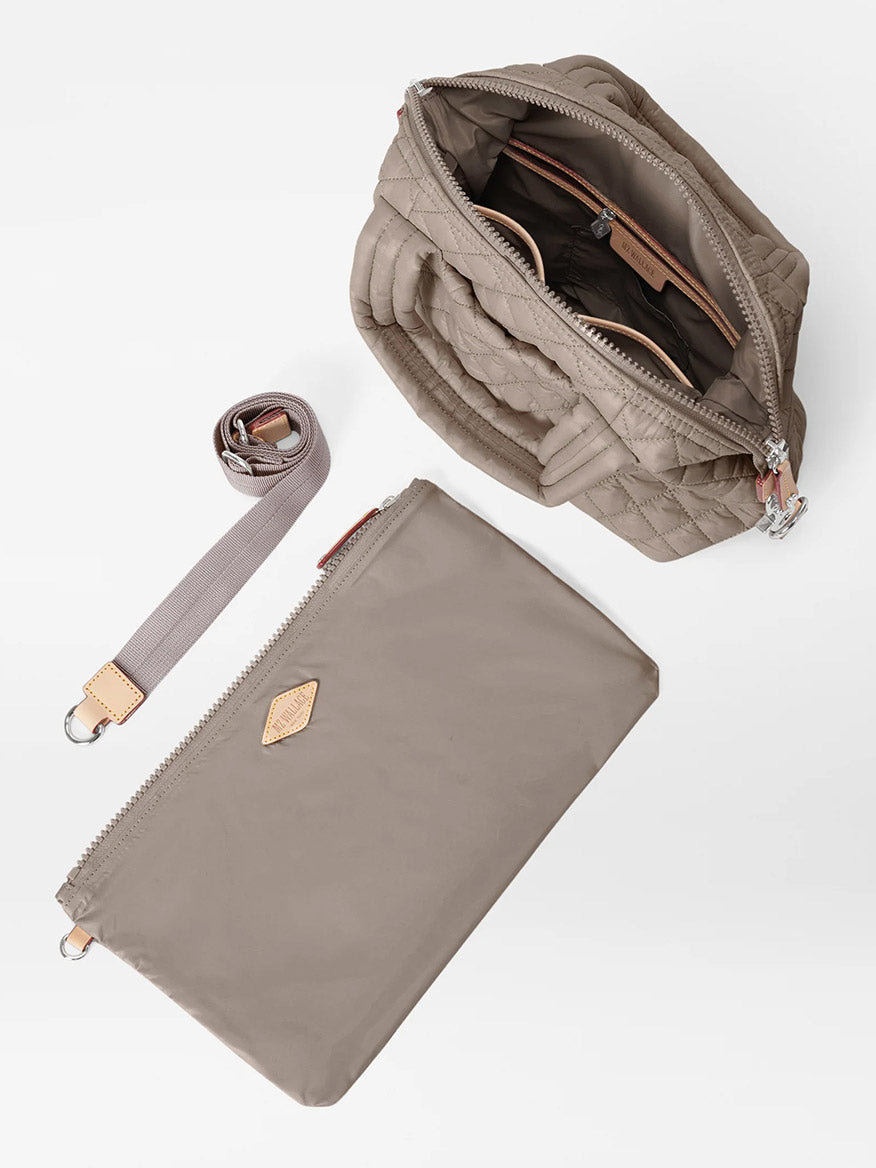 The MZ Wallace Small Sutton Deluxe in Morning Dove Oxford is shown with its interior visible through an open zipper, alongside a matching detachable strap and a flat zippered pouch, all displayed on a white background.