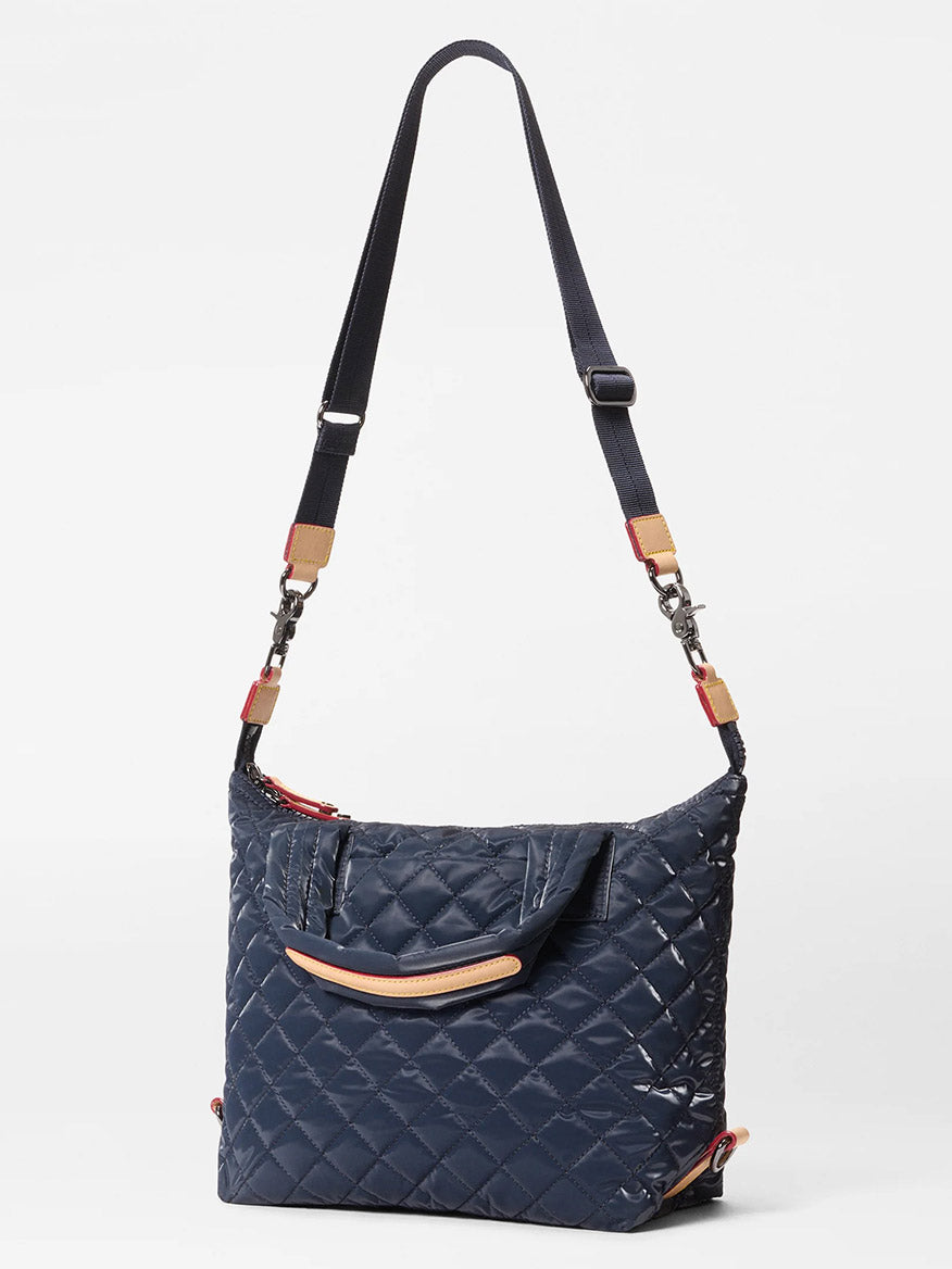The MZ Wallace Small Sutton Deluxe in Ink Liquid Oxford is a navy quilted crossbody bag with adjustable strap, top handles, and Italian leather trim, shown against a plain white background.