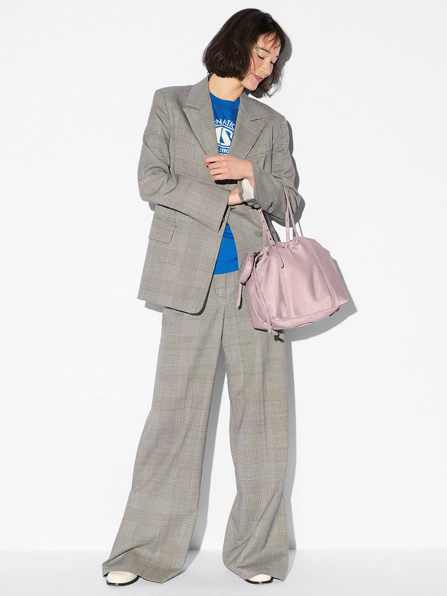 A woman in a gray plaid suit and blue t-shirt holds the MZ Wallace Small Waverly Tote in Quail Bedford with Italian leather trim, looking down against a plain white background.