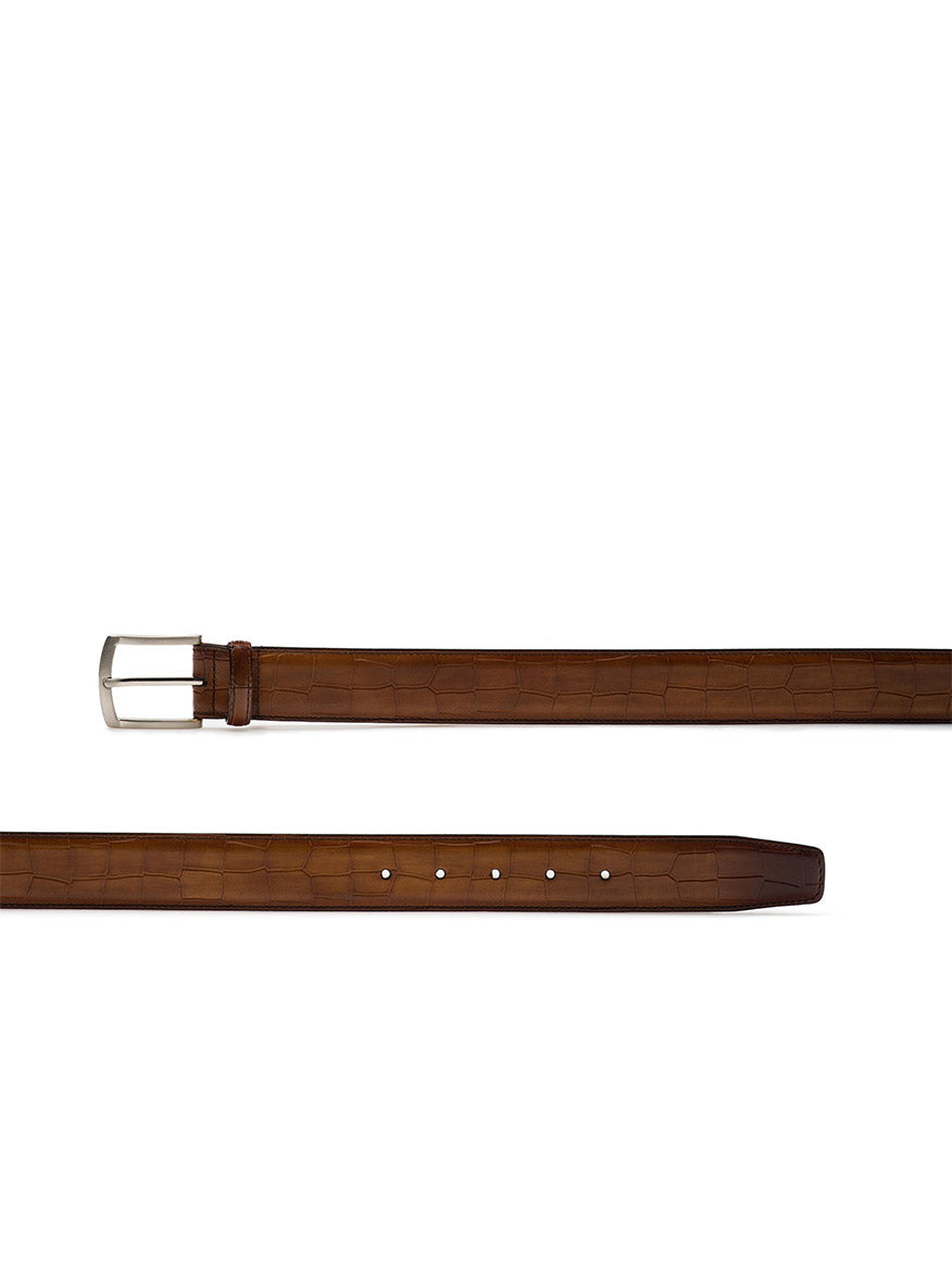 The Magnanni Grabar Belt in Cuero is made of brown calfskin leather, featuring an elegant alligator-embossed pattern, a silver belt buckle, and five adjustment holes.